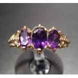 GRADUATED AMETHYST THREE STONE RING the three oval cut amethysts flanked by relief moulded