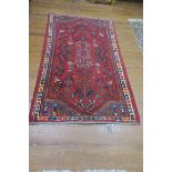 A WOOL RUG, the red ground with central panel filled with palmettes,