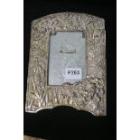 A SILVER PLATED EMBOSSED PHOTO FRAME, of rectangular arched outline embossed with flowerheads,