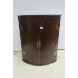 A GEORGIAN MAHOGANY BOWFRONT HANGING CORNER CUPBOARD with brass strap hinges the interior with