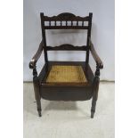 AN EDWARDIAN STAINED WOOD COMMODE ELBOW CHAIR the shaped top rail with baluster splats and scroll