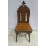 A GOTHIC DESIGN OAK HALL CHAIR with pierced tracery back above a panelled seat on splayed legs