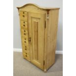 An antique pine cupboard with single panelled door and a bank of six short drawers with brass