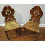 A pair of 19th century oak hall chairs with cartouche-carved and pierced backs, raised on turned and