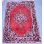 A hand-knotted Persian style rug with central medallion to red ground, with floral spandrels and