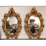 A pair of oval giltwood wall mirrors with carved and pierced scrolling foliate carved frames,