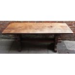 An oak refectory dining table with thick planked top and carved double stretcher to trestle ends