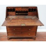 A George III oak bureau, with hinged sloped front enclosing pigeonholes and drawers, above four long