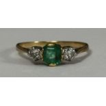 A yellow metal (tests as 18ct gold) ring centrally set with an emerald, flanked by two claw set