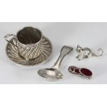 A silver child's spoon together with a white metal pin cushion in the shape of a shoe and a seated