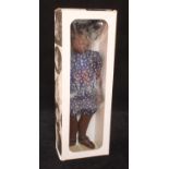 A Sasha 118 Cora Flower Dress doll in blue floral dress and brown sandals, with wrist tag in un-