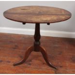 A 19th century stained oak tilt-top table, raised on turned support to down-swept tripod base, top