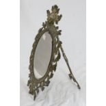 A bevelled oval table mirror in ornately worked brass frame, with floral decoration and lions mask