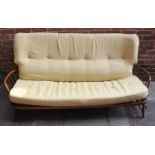 An Ercol three-seater sofa in mid-brown elm finish, with curved stick back, raised on turned