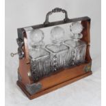 A tantalus with three cut-glass square decanters, lockable cradle