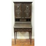 An antique carved and stained oak bureau with cupboard top, enclosed pigeonholes and drawers, raised