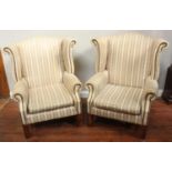 A pair of modern wingback chairs raised on square supports with cream and brown striped upholstery