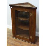 A 19th century stained oak hanging corner cupboard with lockable glazed door enclosing shaped