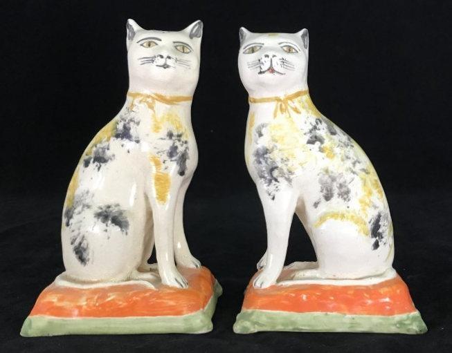 A pair of 19th century Staffordshire pottery figures of seated cats, decorated with patches of ochre