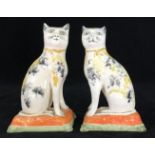 A pair of 19th century Staffordshire pottery figures of seated cats, decorated with patches of ochre