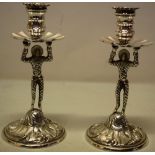 A pair of cast silver tapersticks with Harlequin figure stems, holding up fan fluted drip pans