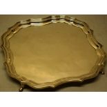 A square silver salver with a raised moulded border, on four scroll splay feet with a Spanish