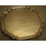 A square silver salver, inscribed, the raised moulded border with incurved corners on scroll legs,