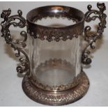 A continental glass cup with chased silver mounts and two cast caryatid scrolling handles, on a leaf