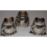 A novelty cast silver frog three piece condiment set, the heads with glass eyes, the hinged lid