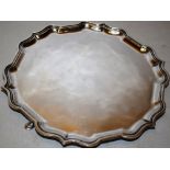 A circular silver salver with a raised 'bath' border, on three scroll legs to hoof feet, 10.25in (