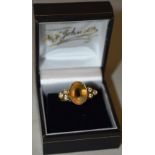 A citrine oval stone ring, flanked by six small diamonds, in a gold coloured metal modern setting.