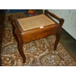 A cane seated Satinwood framed music Stool with music compartment and turned carrying handles to