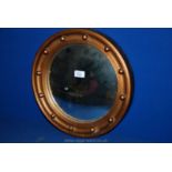 A circular convex wall mirror with a wooden framed with a gold- coloured rim.
