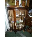 A bow fronted Oak china Display Cabinet standing on brief legs with ball and claw feet,