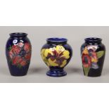 Three blue ground Moorcroft bud vases one in the anemone design, one with hibiscus design and the