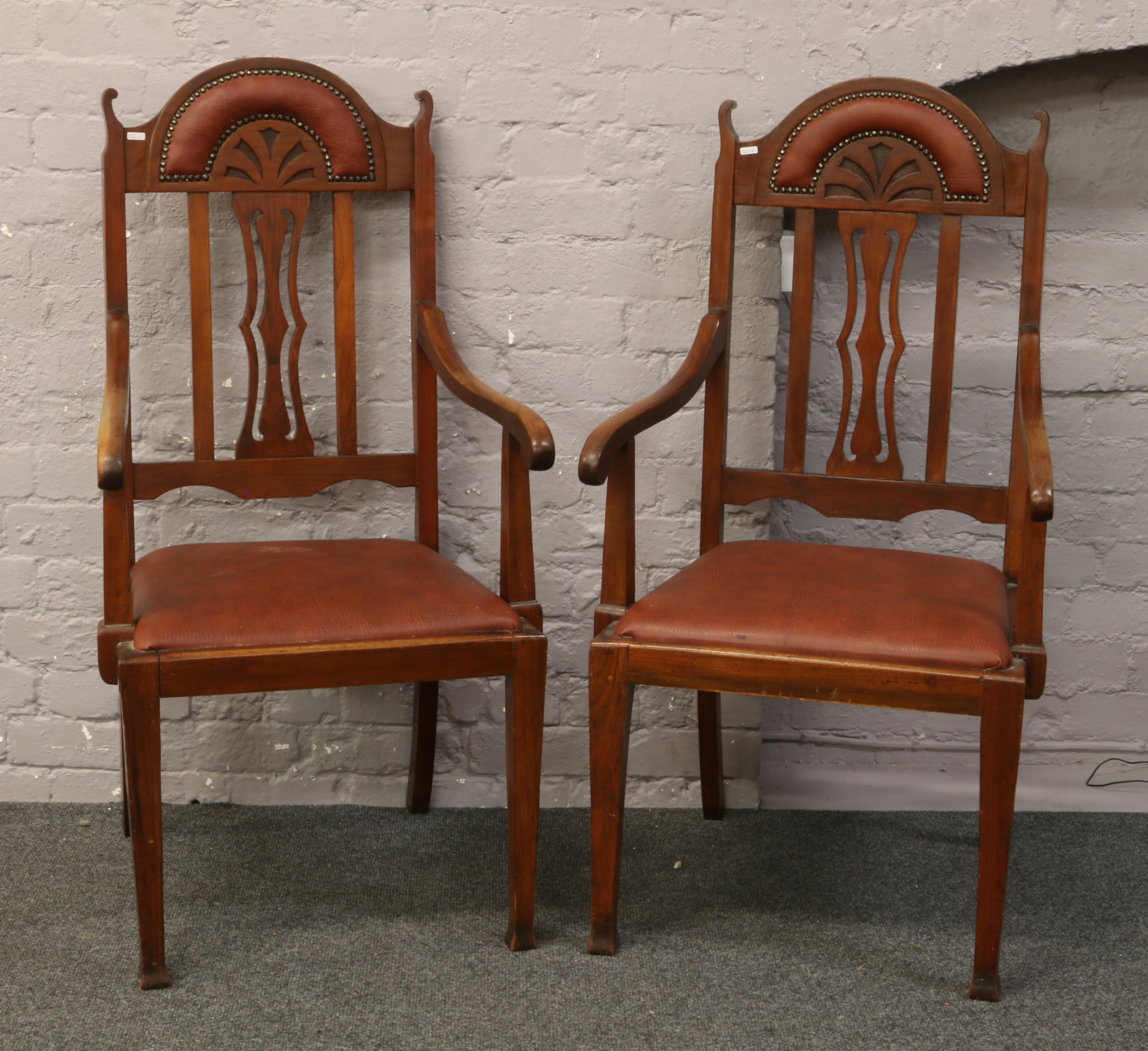 A pair of carved mahogany armchairs with leatherette and studded upholstery.