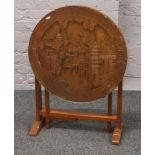 An oriental carved tilt top occasional table with glass top raised on gate leg supports.