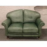 A green leather two seat sofa raised on turned castered supports.