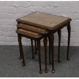 A nest of three carved mahogany occasional tables with tooled leather inlay.