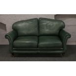 A green leather three seat sofa raised on brass castered turned mahogany legs.