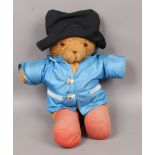A large teddy bear dressed in rain coat and black hat.
