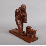 An Inuit style carving depicting a figure of a man wearing snow shoes walking with a dog,