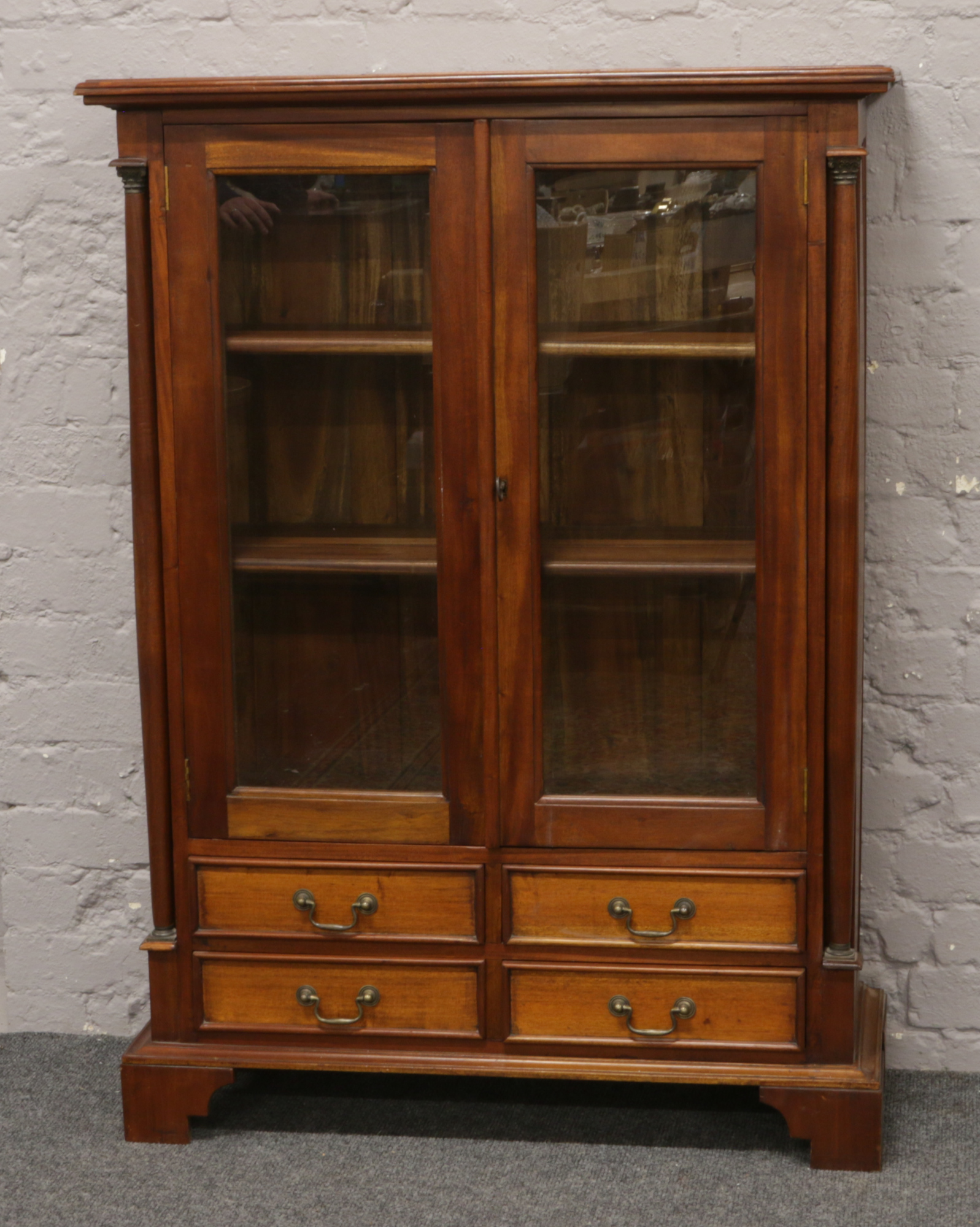 A mahogany glass front bookcase over four drawer base.