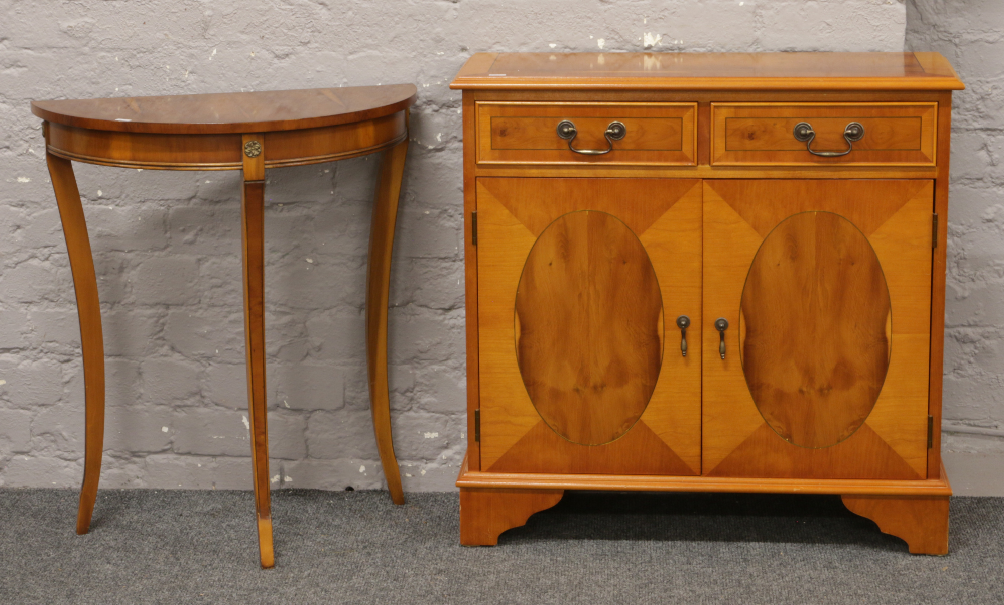 A yew wood two drawer cupboard raised on bracket feet along with a demi lune side table.