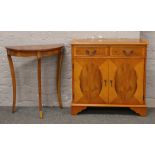 A yew wood two drawer cupboard raised on bracket feet along with a demi lune side table.