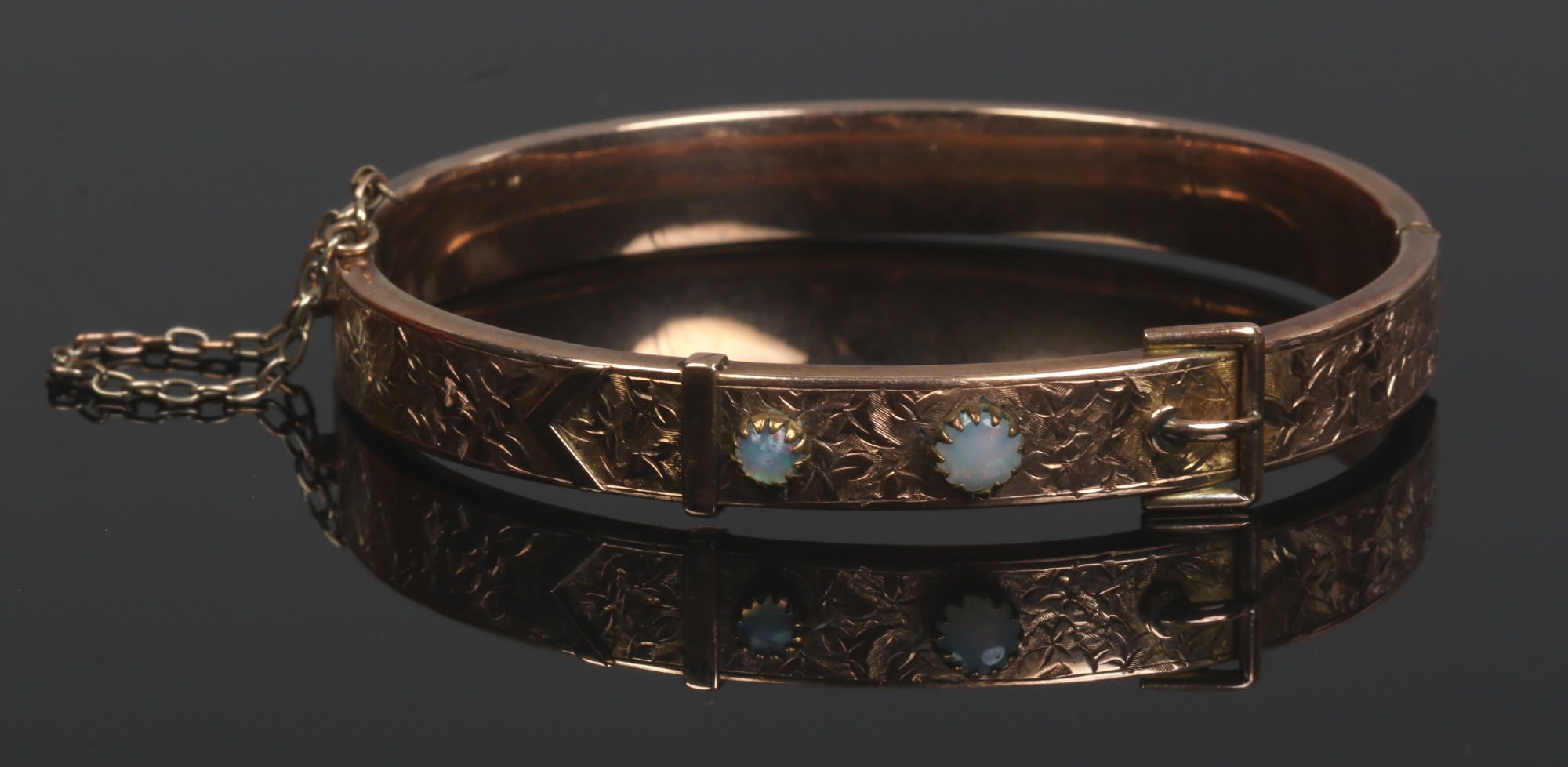 A Victorian 9ct gold bangle. Formed as a belt, chased with scrolling ivy leaves and set with an opal