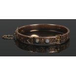 A Victorian 9ct gold bangle. Formed as a belt, chased with scrolling ivy leaves and set with an opal