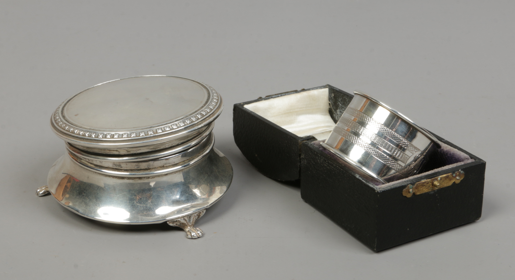 A silver ring box raised on paw feet assayed Birmingham 1924 and a cased silver serviette ring,