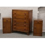 A mid 20th century oak veneered chest of five drawers along with two similar bedside cabinets with