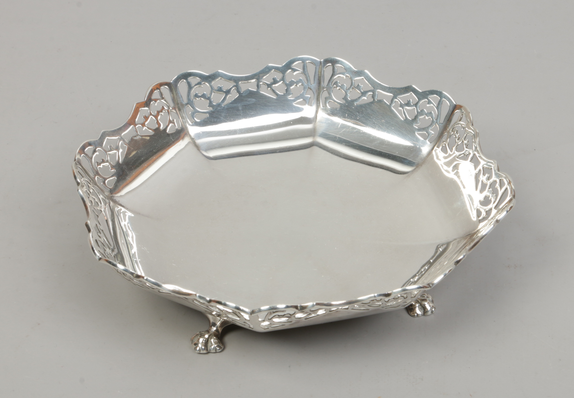 A George V octagonal silver bon bon dish with pierced rim and raised on four claw feet, assayed